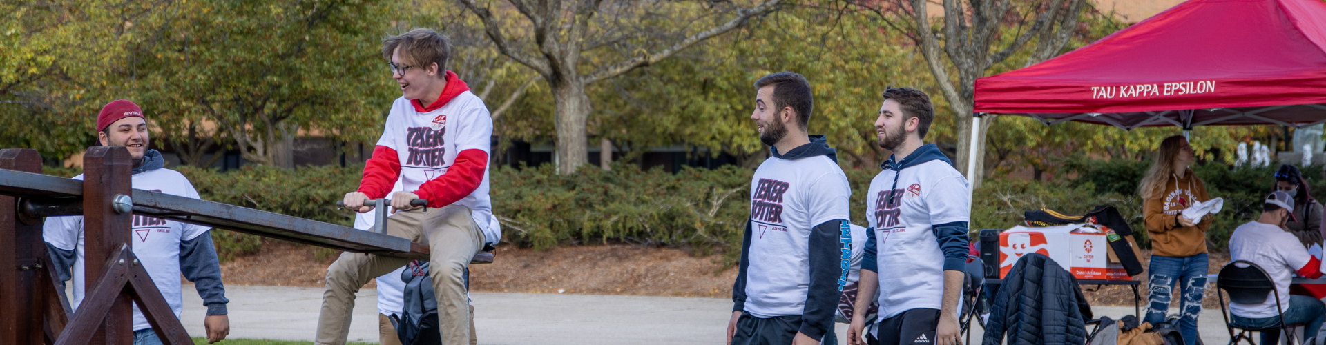 Students watching another student on the teeter totter for the Tau Kappa Epsilon event for charity.